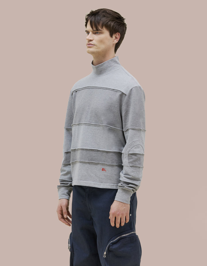 A relaxed-fit Eckhaus Latta long sleeve turtleneck with a two way metal zipper along the center back. Stripes are assembled from individual strips, finished externally to echo our signature lapped seams. Red "EL" logo embroidery at the lower left abdomen.