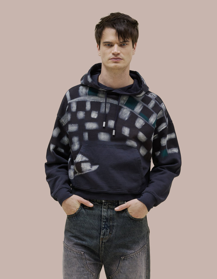  Made of brushed French terry with a relaxed, cropped fit. Garment dyed in deep navy and finished with a checkered spray design across the body, shoulders, and hood. Features a glossy "Eckhaus Latta" logo on the shoulder.
