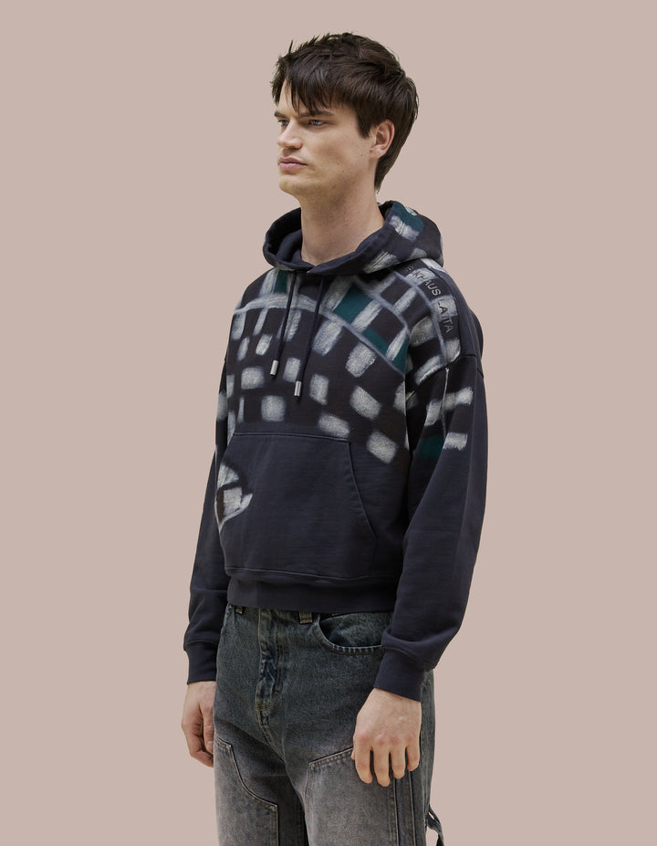  Made of brushed French terry with a relaxed, cropped fit. Garment dyed in deep navy and finished with a checkered spray design across the body, shoulders, and hood. Features a glossy "Eckhaus Latta" logo on the shoulder.