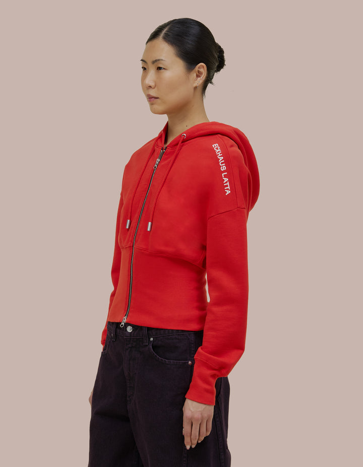 Our classic Eckhaus Latta snatched hoodie style in a brushed French terry with a fitted ribbed hem band. Garment dyed in solid red, finished with a glossy off-white "Eckhaus Latta" logo on the shoulder.